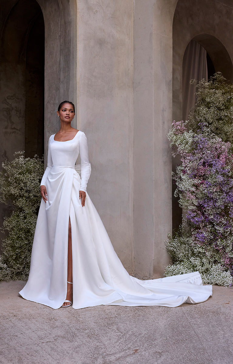 Woman in a white wedding dress standing in front of a stone wall with floral decorations.