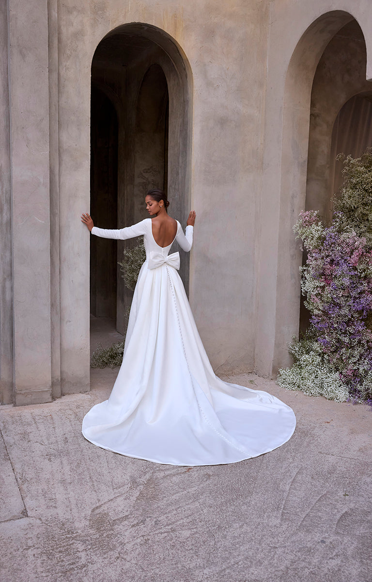 Woman in a white wedding dress standing in front of stone arches with floral decorations.
