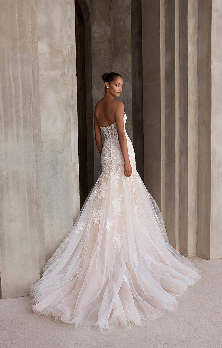 Woman in a white wedding dress standing against a neutral wall.