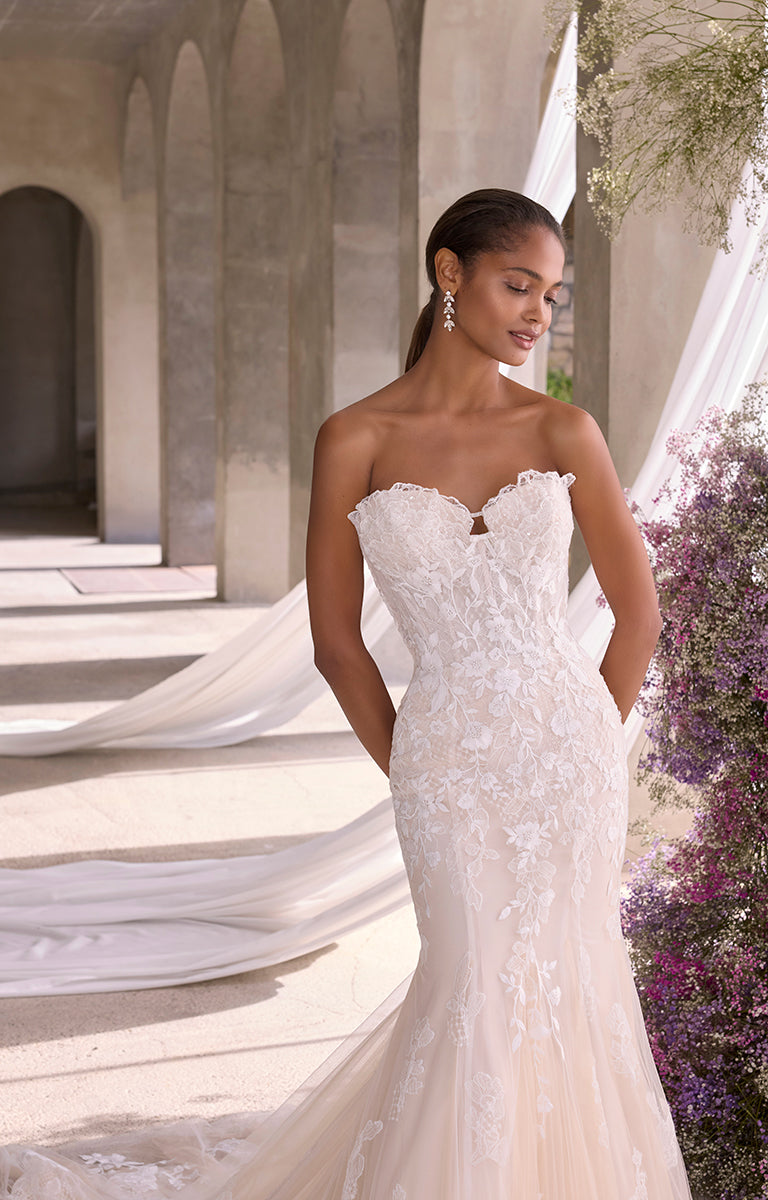 Woman in a strapless wedding dress standing in an outdoor setting with columns and flowers.