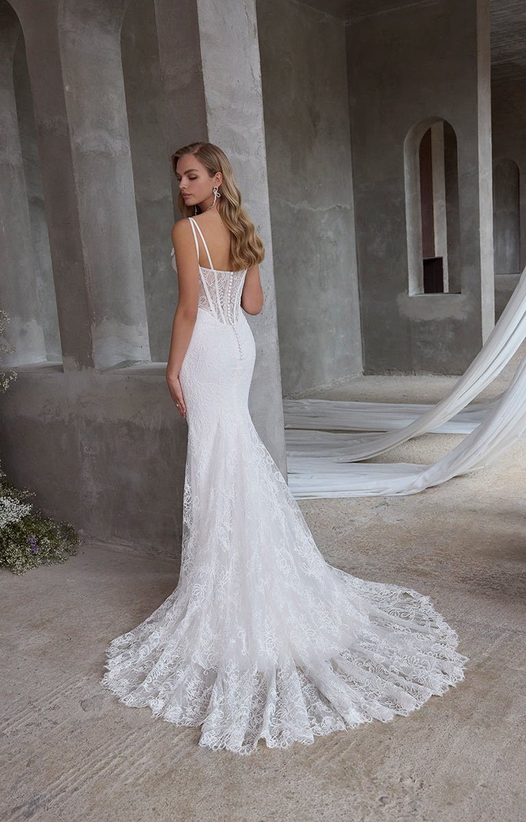 Woman in a white lace wedding dress standing in an architectural setting.