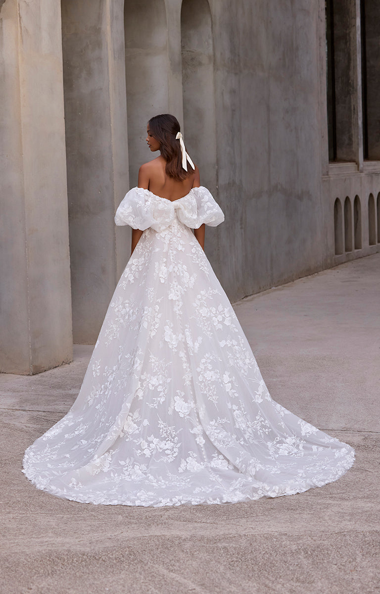Woman in a white floral wedding dress standing in an architectural setting.