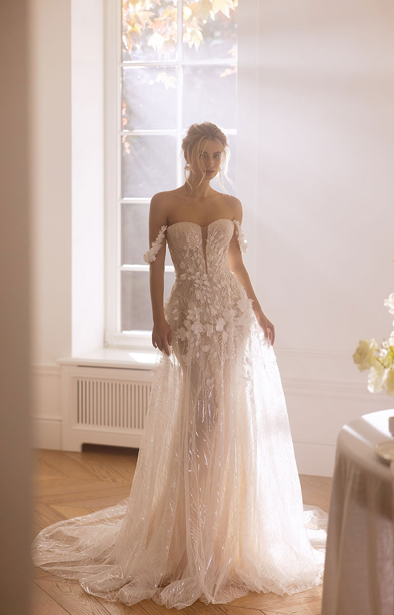 Woman in a white wedding dress standing in a room with a large window.
