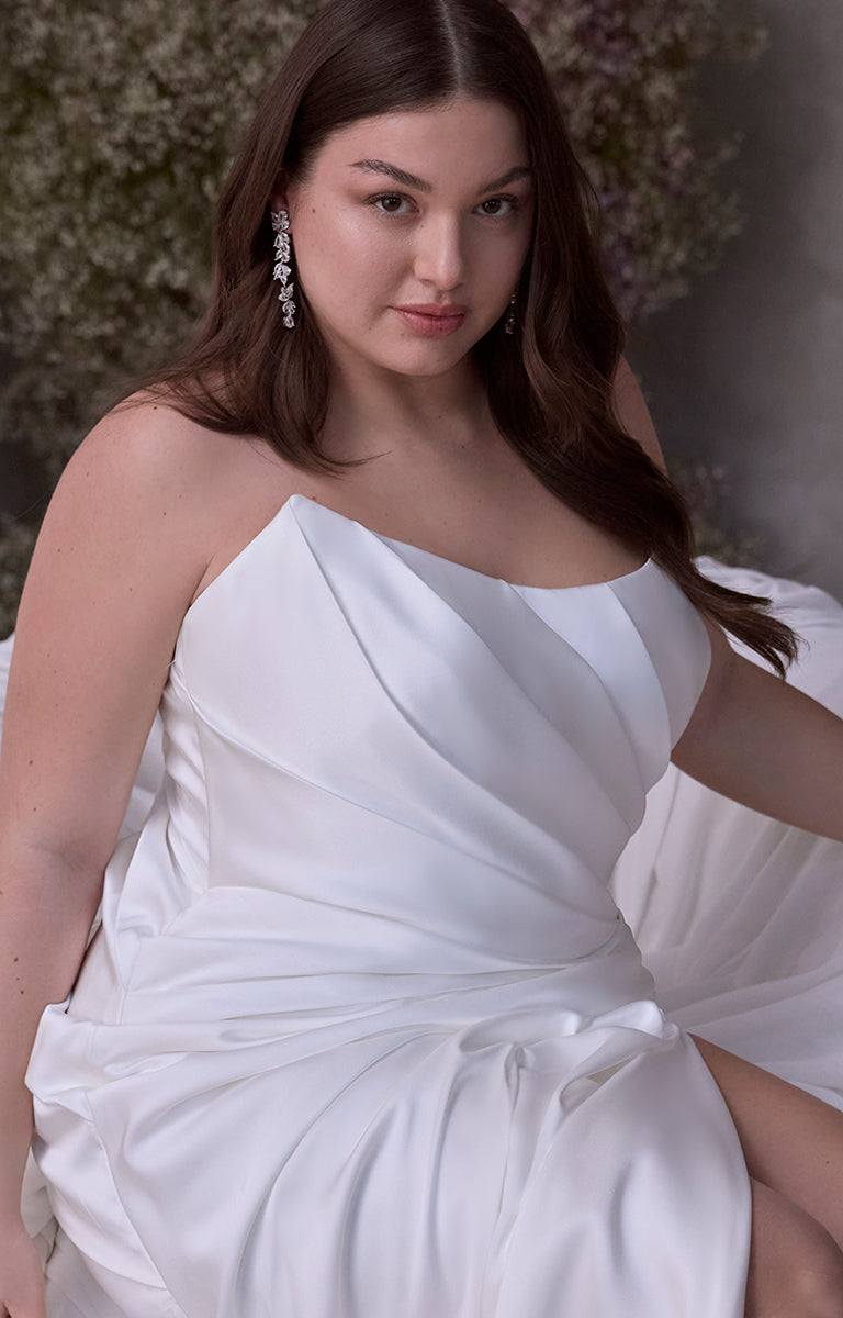 Woman wearing Vipsania by Morilee Julietta - a white one-shoulder dress with a blurred floral background