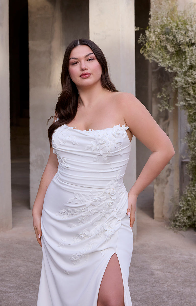 Woman in Rea by Morilee Julietta - a white strapless dress standing outdoors with columns and greenery in the background