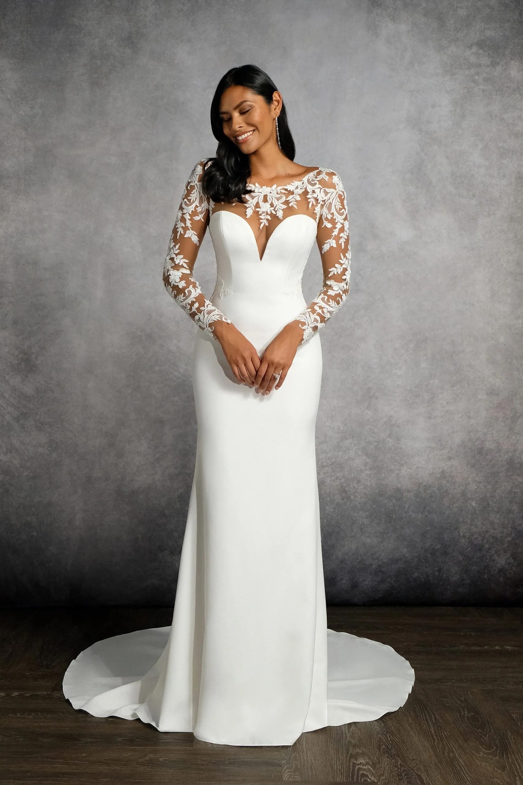 Woman wearing a white wedding dress with lace sleeves against a gray background