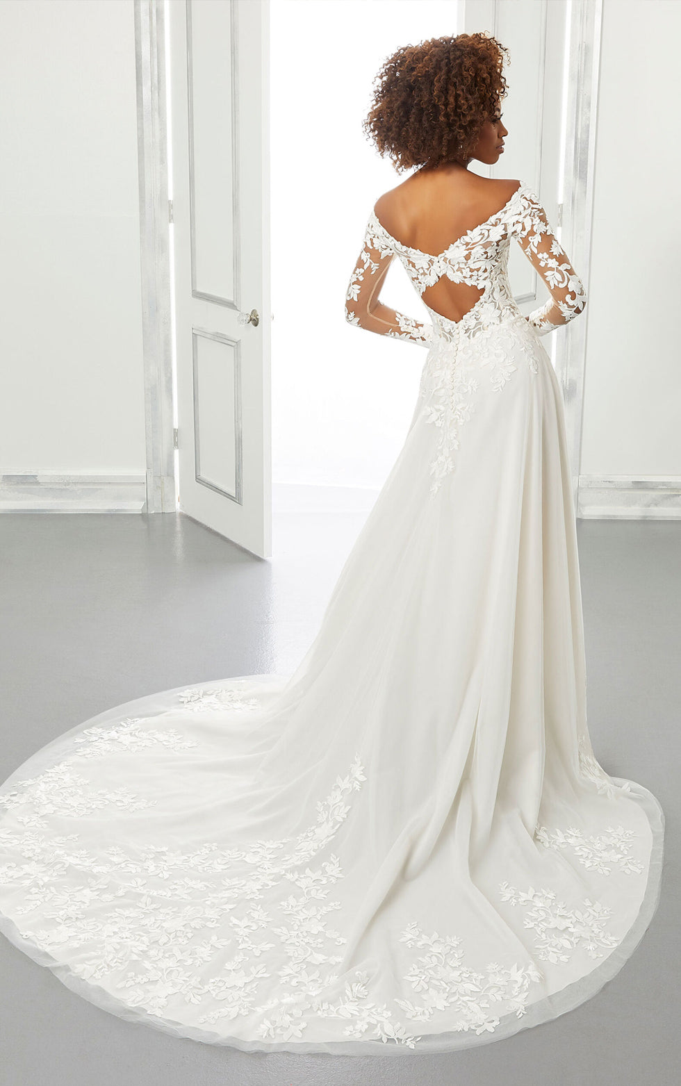 Woman wearing a white wedding dress with lace details in a minimalistic setting.