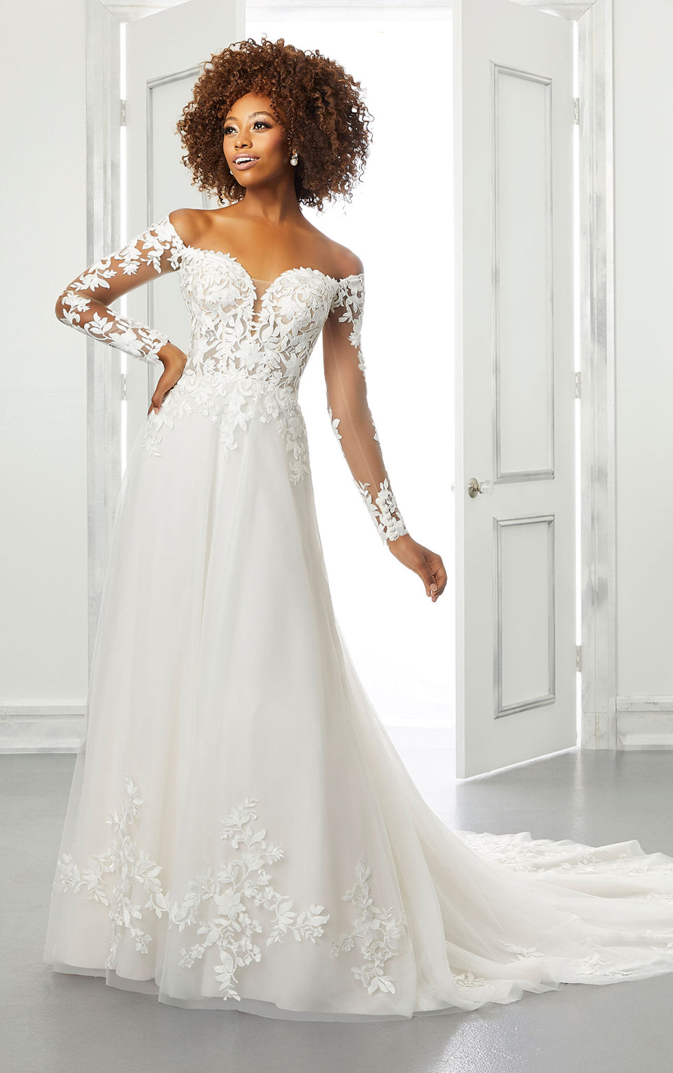 Woman wearing a white wedding dress with lace details in a bright room.