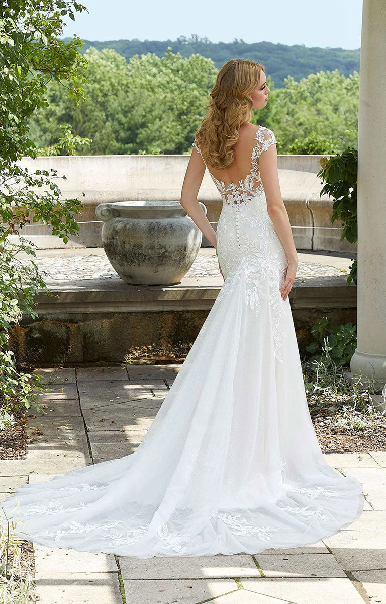 Woman in Daisy Wedding Dress by Morilee - Style 5946 – Botanical Lace Mermaid Gown with Illusion Neckline standing outdoors with greenery in the background