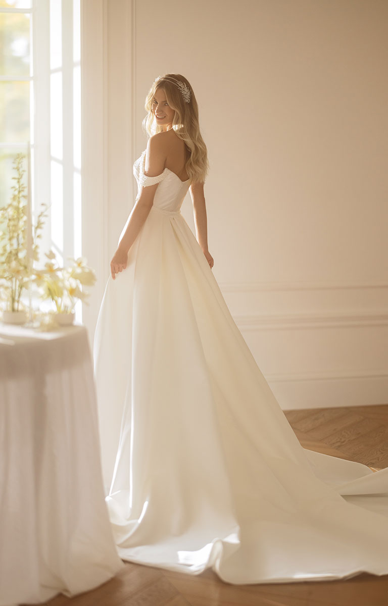 Woman in a white wedding dress standing in a softly lit room with a neutral color palette.