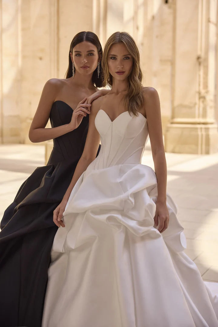 Two women, one in a black dress and the other in a white wedding gown, posing together.
