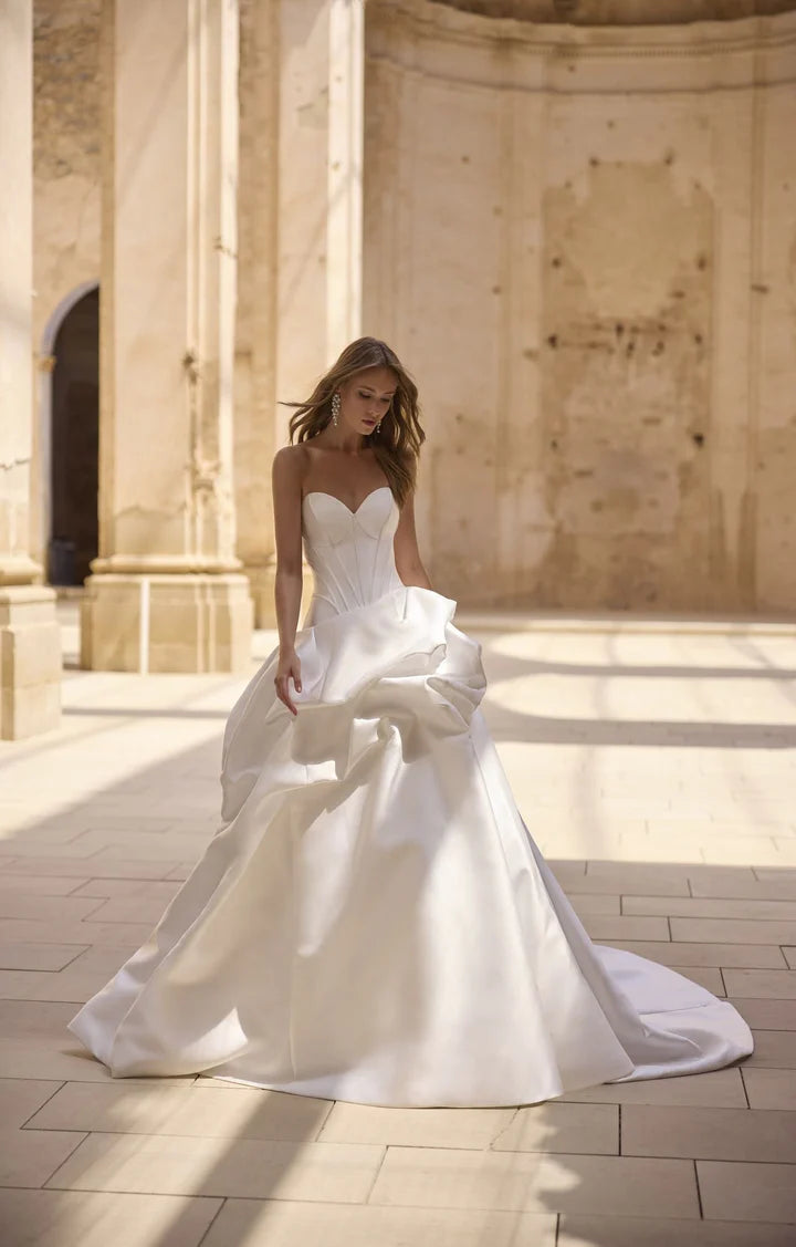 Woman in a white wedding dress standing in a sunlit stone courtyard.