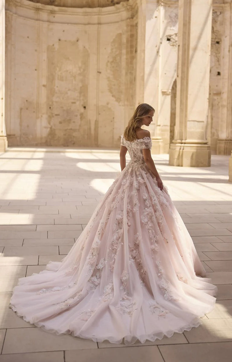 Woman in Hideko by Veni Infantino Bridal - Botanical Ball Gown Wedding Dress with 3D Floral Appliqués standing in a sunlit architectural setting.