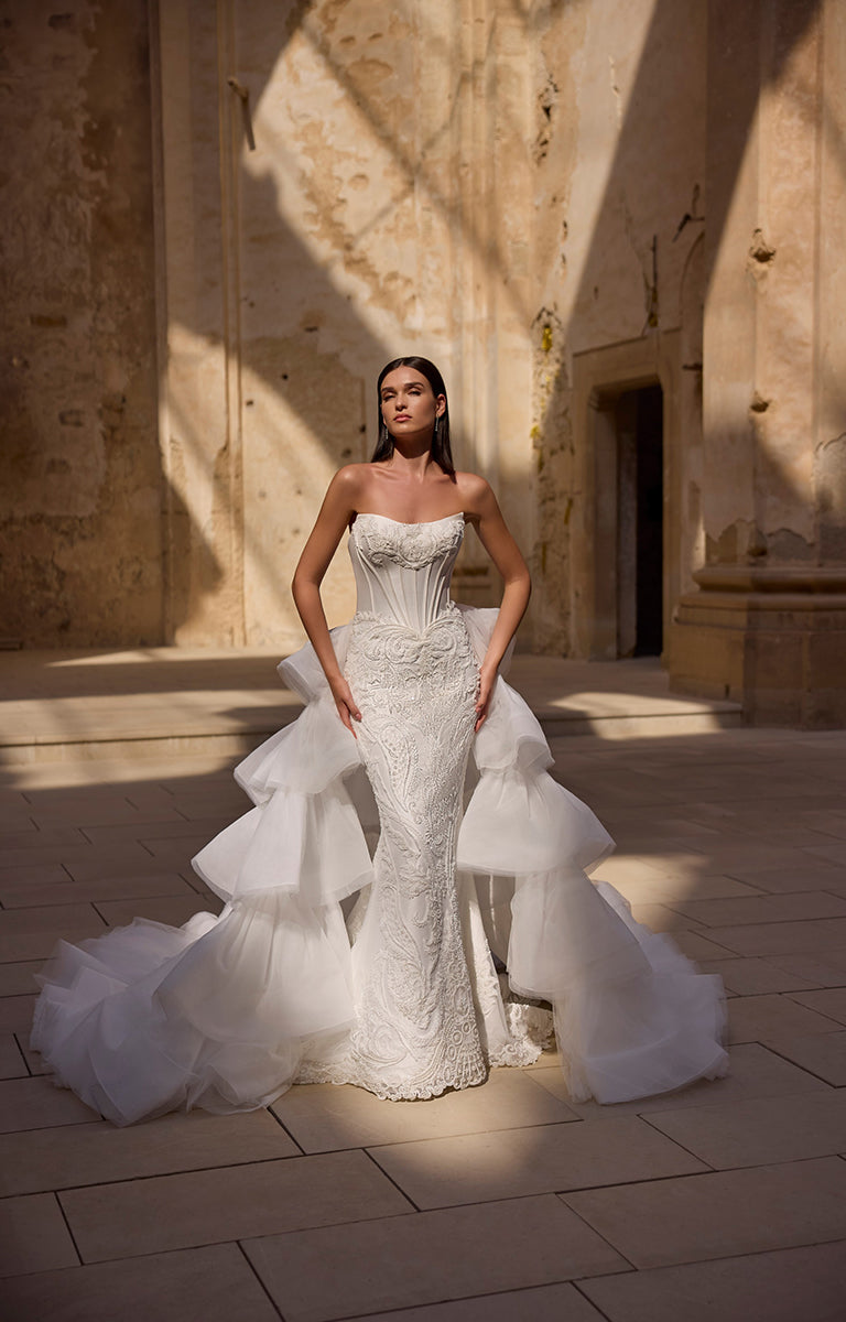 Woman in a white wedding dress standing in a sunlit courtyard.