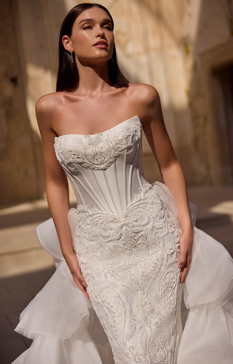 Woman wearing a white strapless embroidered wedding dress against a neutral background