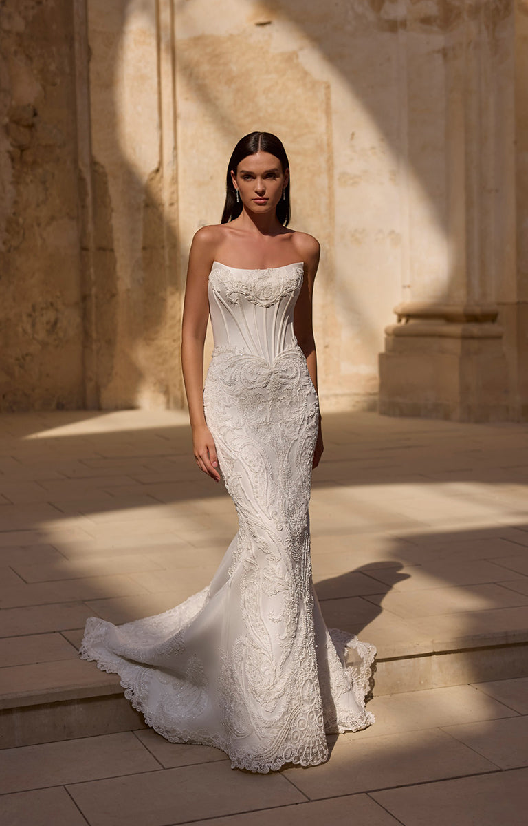 Woman in a white lace wedding dress standing in a sunlit stone courtyard.