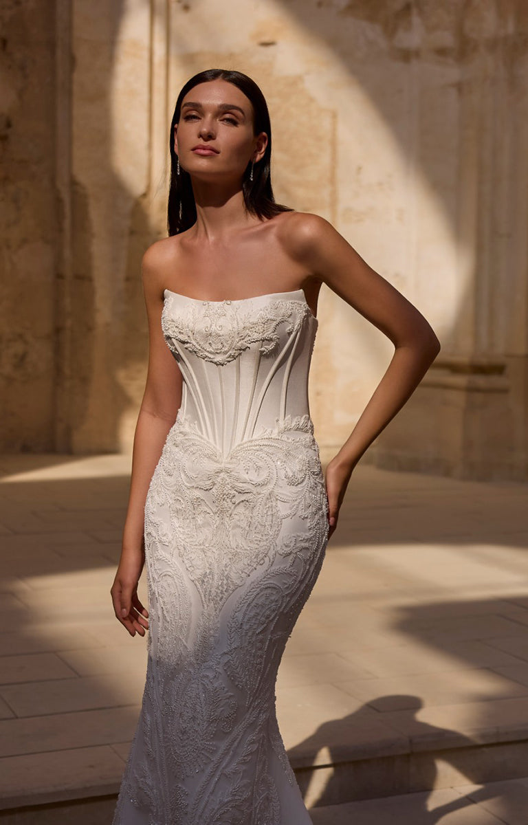 Woman wearing a white strapless gown with intricate detailing in an outdoor setting.