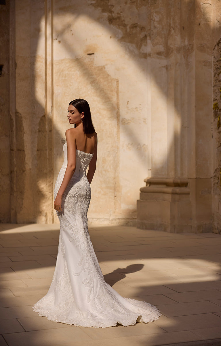 Woman in a white wedding dress standing in a sunlit stone hallway