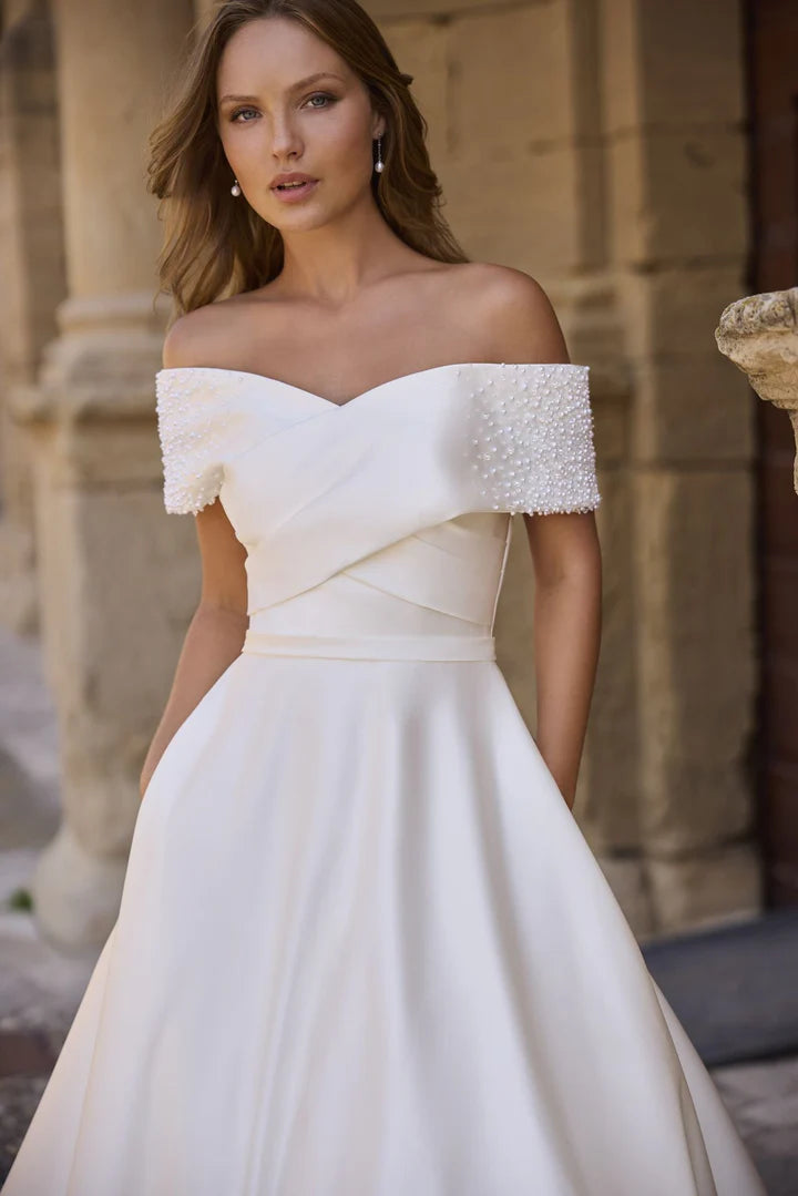 Woman wearing a white off-shoulder gown with textured bodice in an outdoor setting.