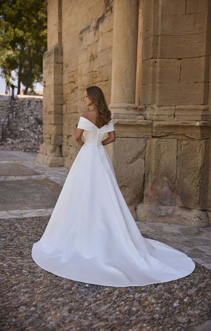 Woman in a white wedding dress standing in front of a stone building.