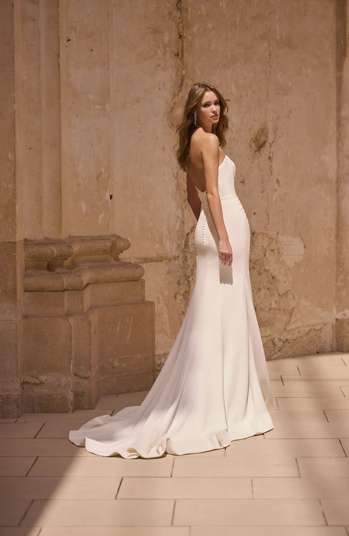 Woman in a white wedding dress standing against a stone wall.