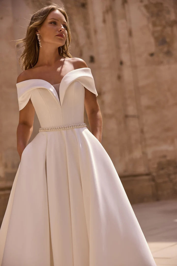 Woman wearing a white off-shoulder dress with a textured wall background