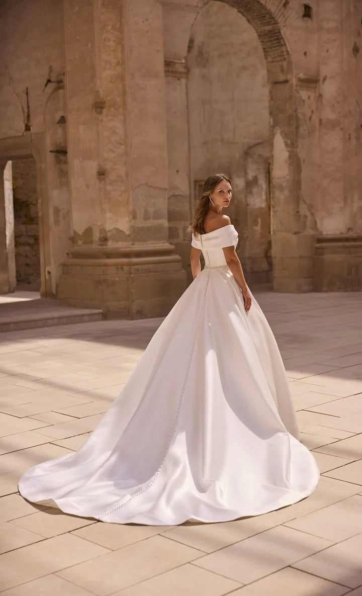 Woman in a white wedding dress standing in front of ancient stone architecture.