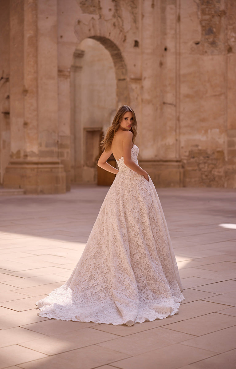 Woman in a white lace wedding dress standing in front of an ancient stone archway.