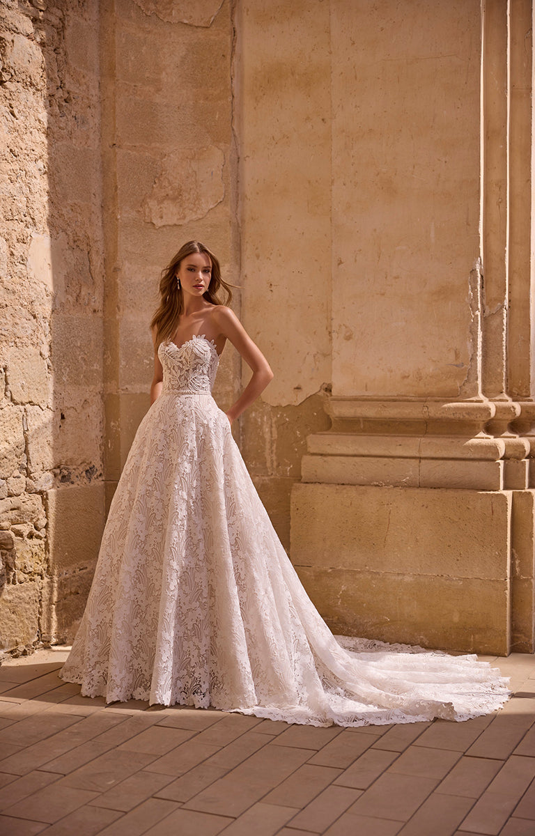 Woman in a white lace wedding dress standing against a stone wall.