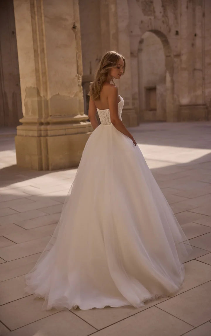 Woman in a white wedding dress standing in an outdoor setting with stone architecture.