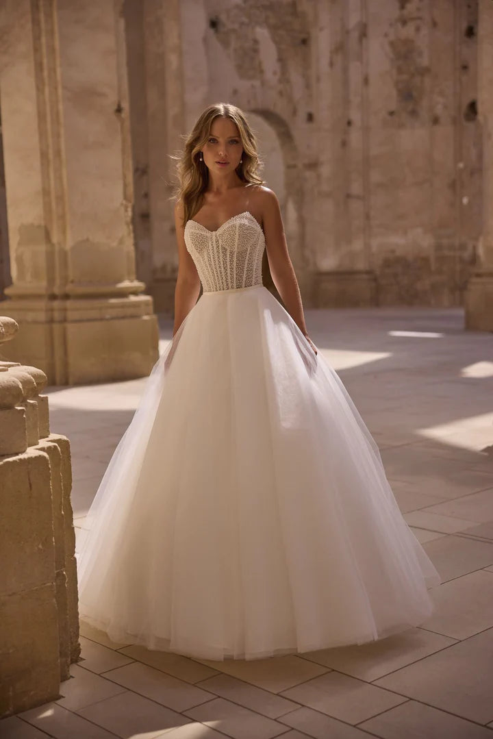 Woman in a white wedding dress standing in an outdoor setting with stone architecture.
