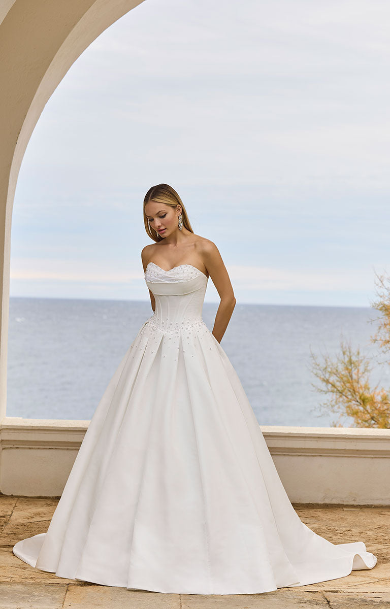 Woman in 63125 Hania by Veni Infantino Bridal - Strapless Taffeta Ball Gown with Beaded Bodice standing by a scenic ocean view.