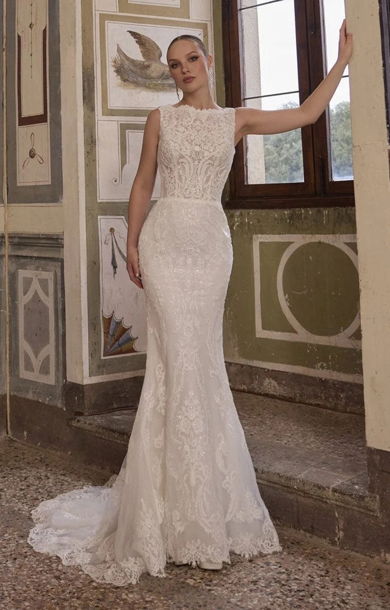 A woman models Veni Infantino Algarve 63332 - Fitted Lace Wedding Dress with High Illusion Neckline, Sparkle and Detachable Belt with a fitted bodice, sheer lace overlay, and a long train in an ornate indoor room with classical wall decor and windows.
