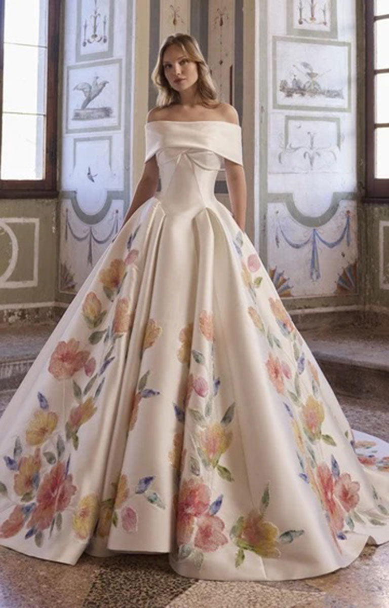 Veni Infantino Arabella 63364 - Strapless Floral Ballgown Wedding Dress with Pleated Skirt with a structured bodice and a voluminous skirt decorated with large watercolor-style floral prints in pink, yellow, and green, worn by a model in an ornate interior room.