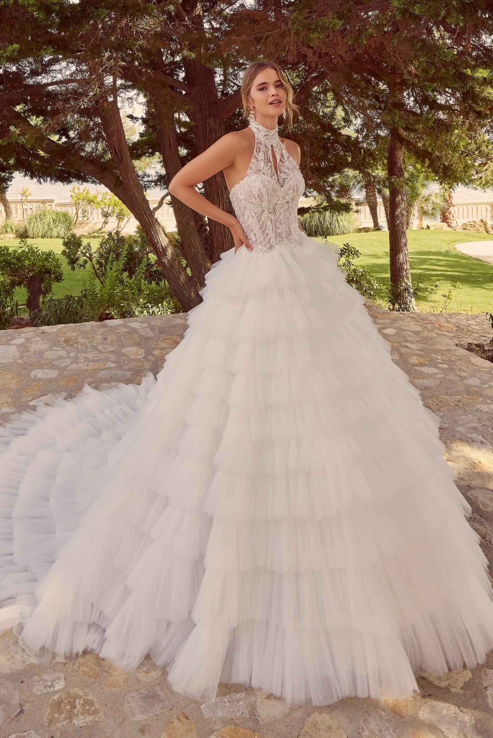 Woman in Zerlina A 69928A by Veni Infantino - Beaded Tulle A-Line Ball Gown with Convertible Neckline standing outdoors with trees and grass in the background