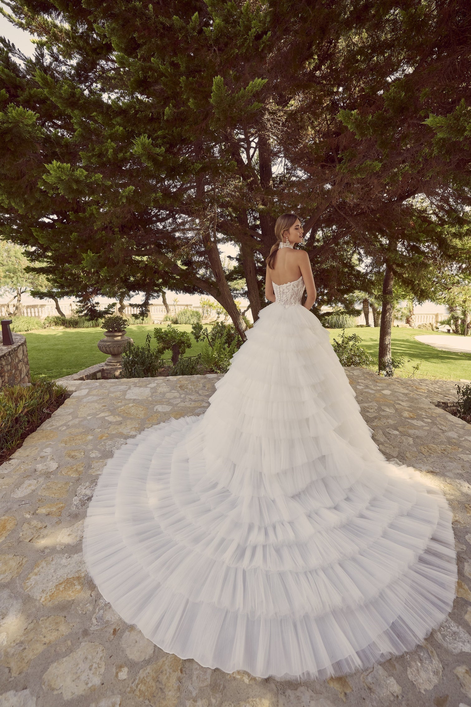 Woman wearing Zerlina A 69928A by Veni Infantino - Beaded Tulle A-Line Ball Gown with Convertible Neckline showcasing the rear of the dress and train.