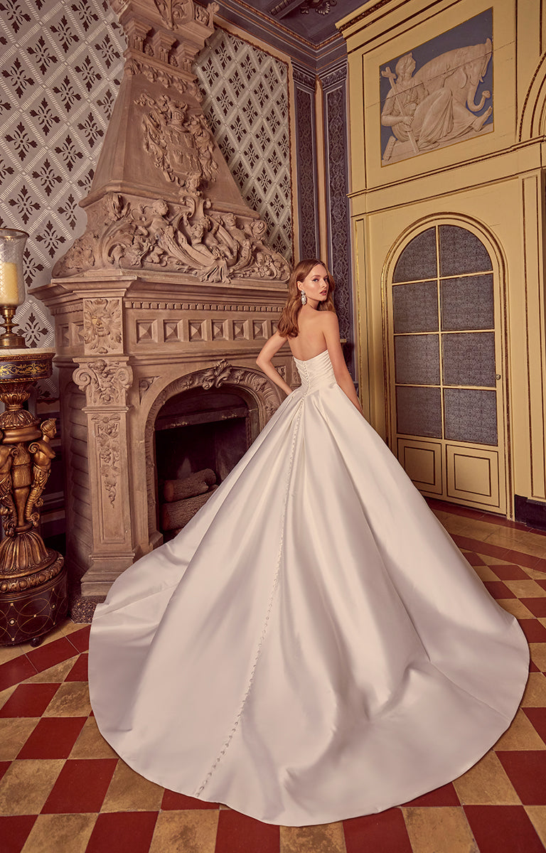 Woman in a white wedding dress standing in an ornate room with a fireplace.