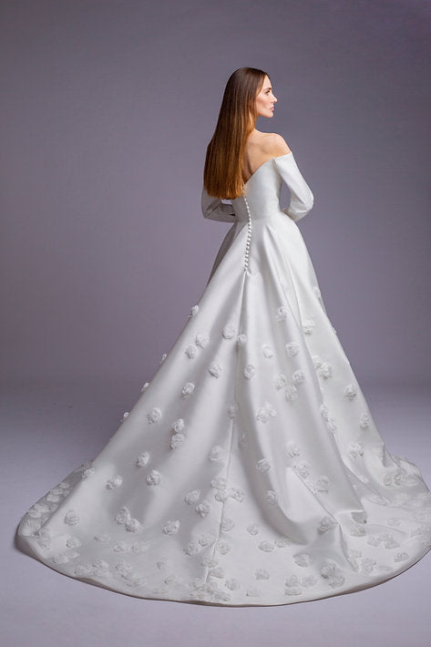 Woman wearing a white wedding dress with floral details on a gray background