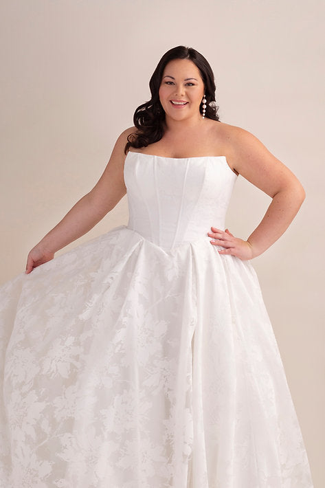 Woman wearing a strapless white wedding dress against a plain background