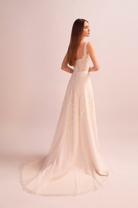 Woman wearing a white wedding dress with intricate detailing on a light pink background