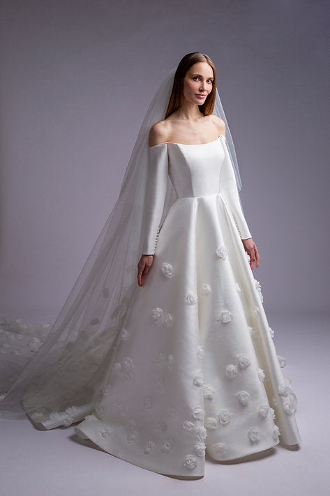 White wedding dress with long sleeves and floral details on a plain background