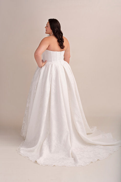 Woman wearing a strapless white wedding dress against a beige background