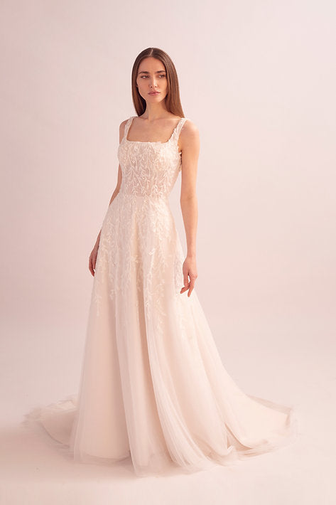 Model wearing a white lace wedding dress on a light pink background