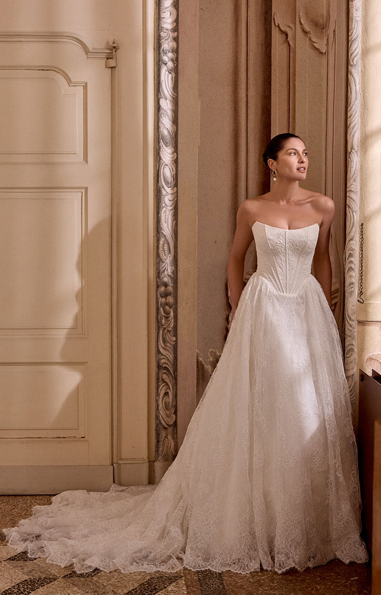 Woman in Leighton 88468 by Justin Alexander - Corded Lace A-Line Wedding Dress with Basque Waist standing in an elegant room with ornate decor.