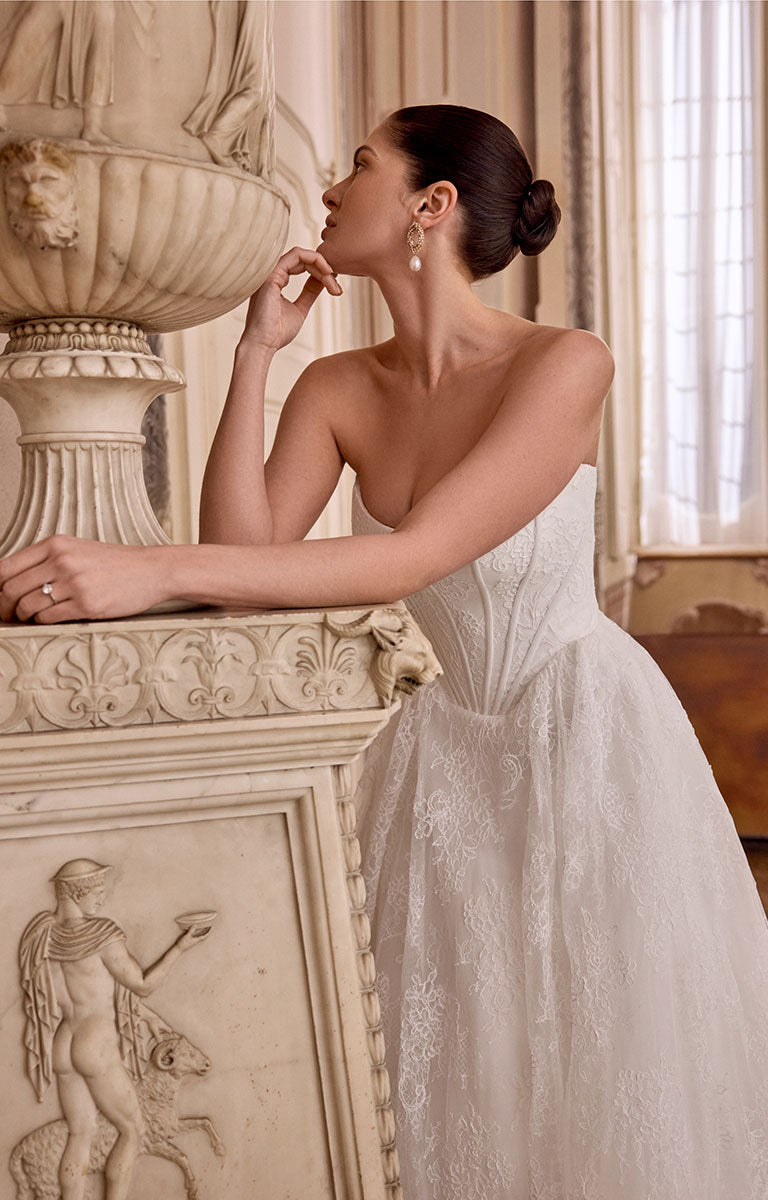 Woman in Leighton 88468 by Justin Alexander - Corded Lace A-Line Wedding Dress with Basque Waist standing in an elegant interior setting.