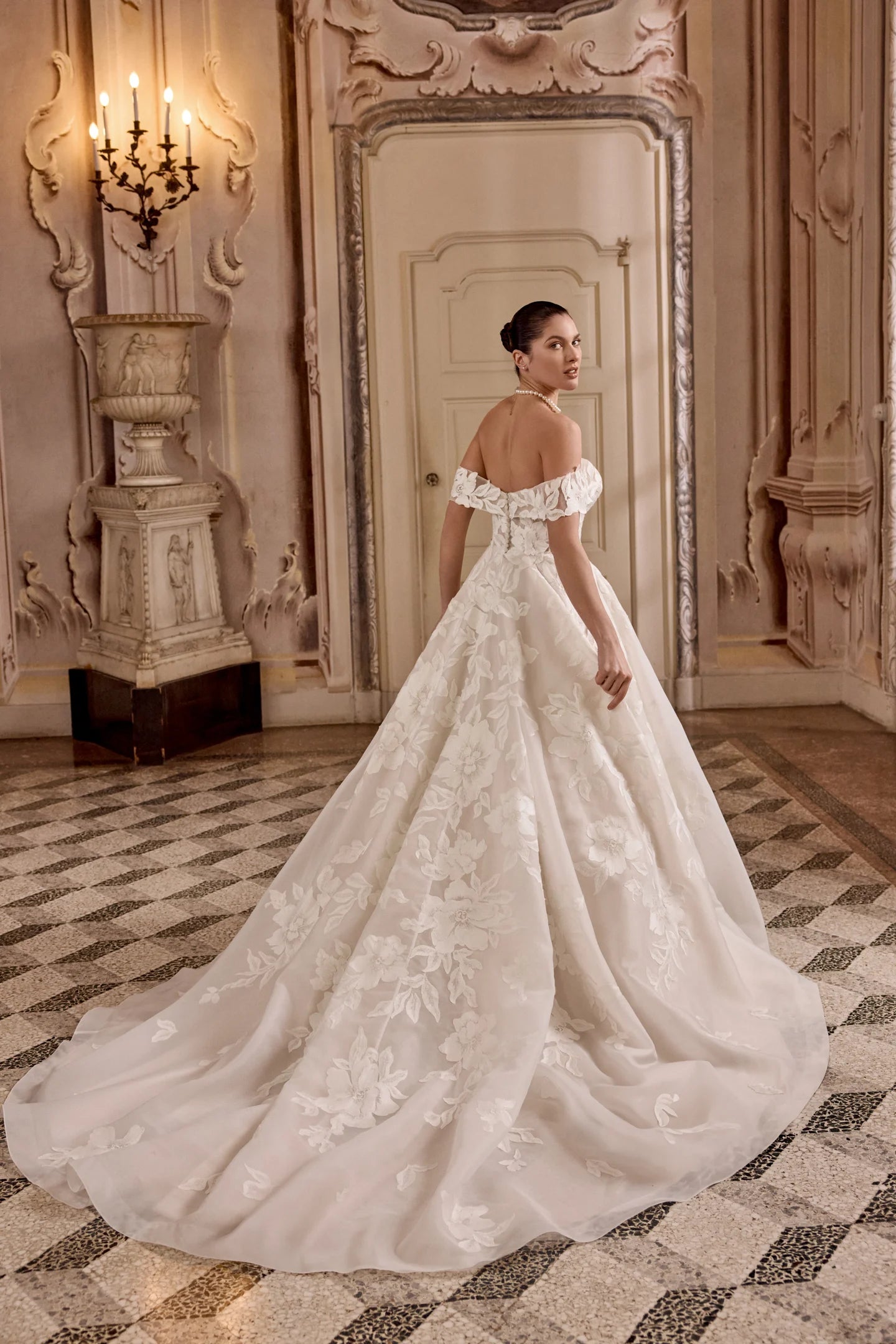 Woman in a white wedding dress standing in an ornate room with a large mirror.