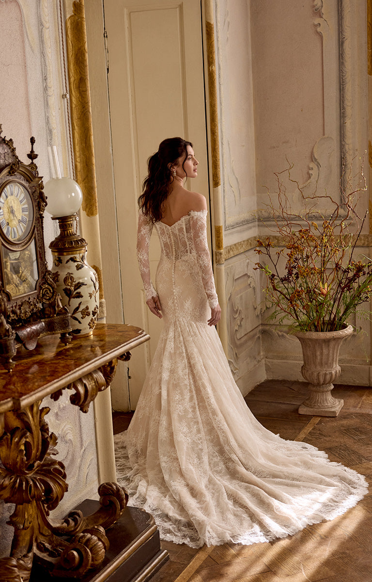 Woman in a white lace wedding dress standing in an elegant room with decorative elements.