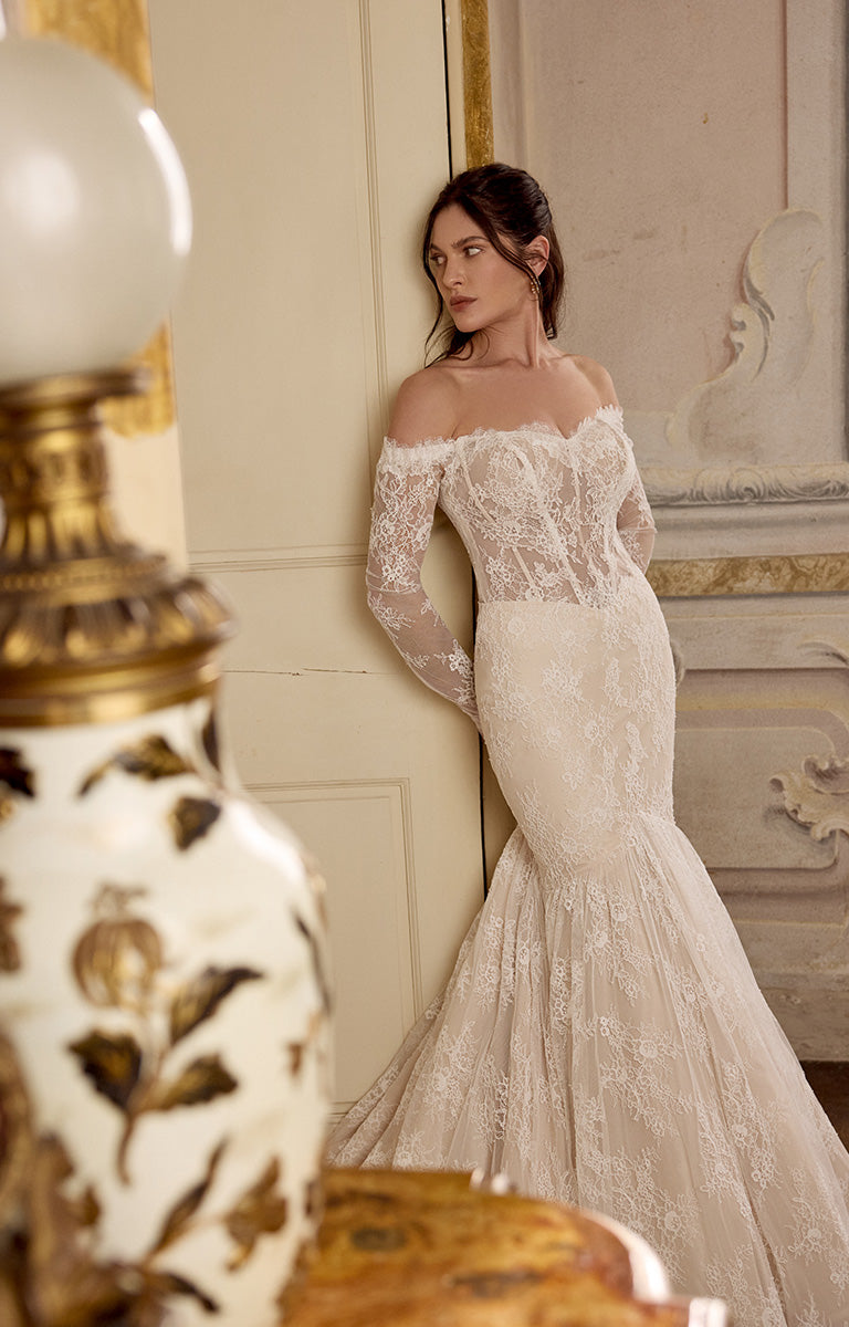 Woman in a lace wedding dress standing in an elegant room.