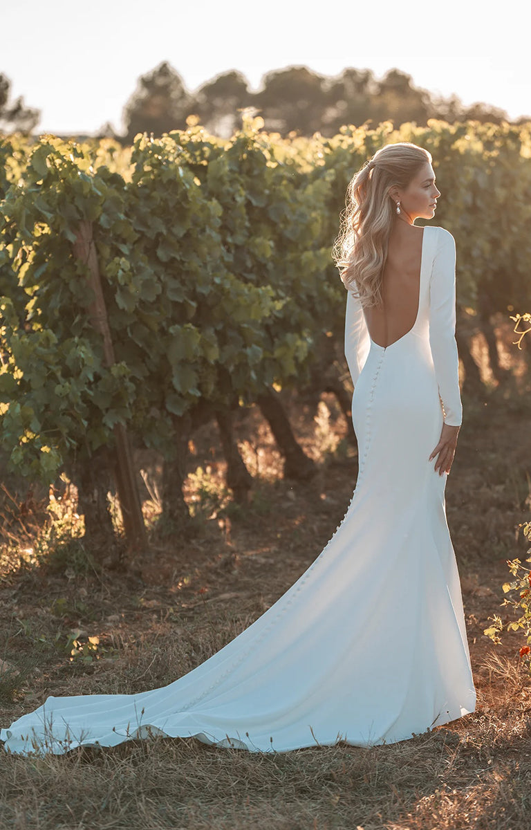 Woman in A1313LS by Allure Bridals - Long Sleeved Stretch Crepe Sheath Wedding Dress standing in a vineyard