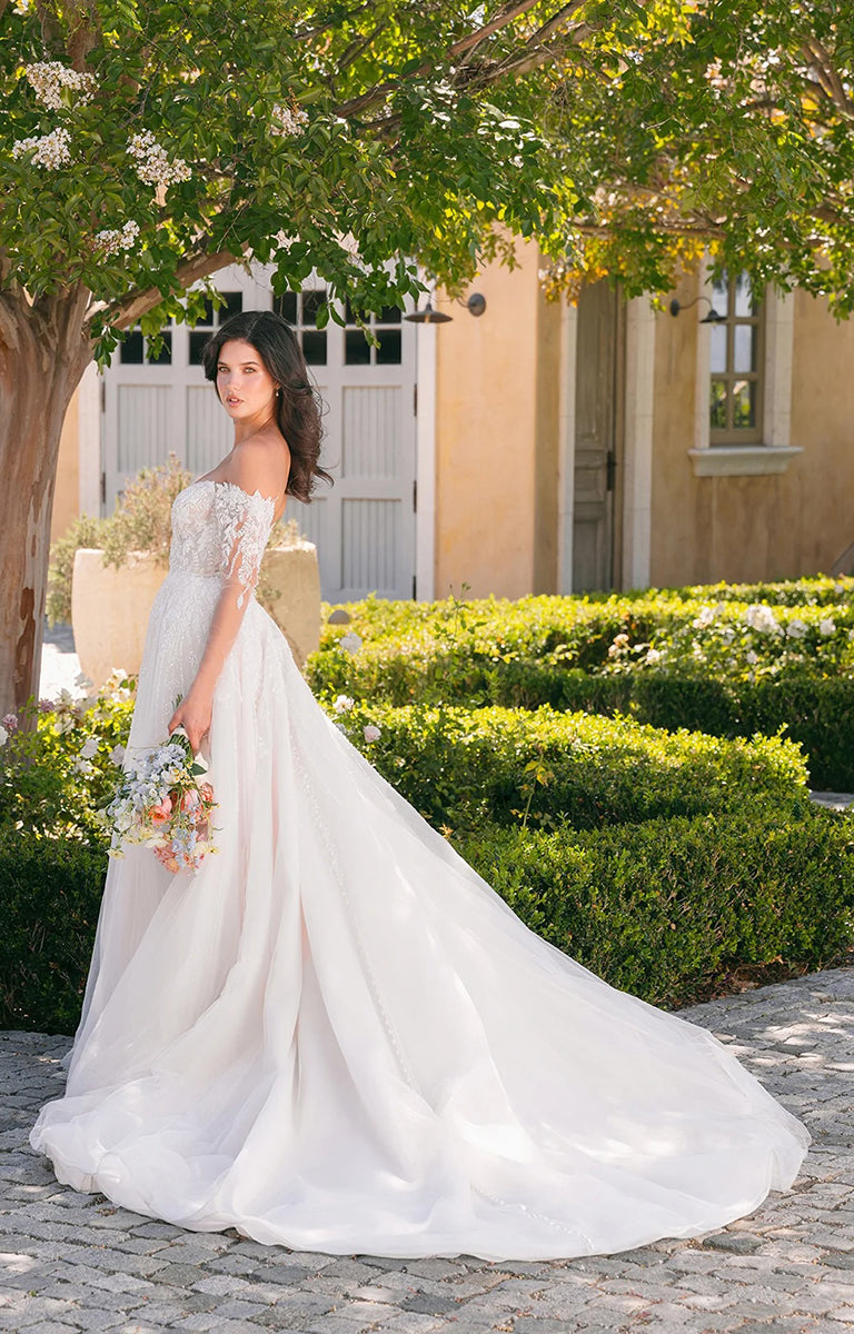 Woman in A1418 by Allure Bridals - Beaded Lace Ball Gown Wedding Dress with Glitter Tulle standing outdoors with greenery and a building in the background